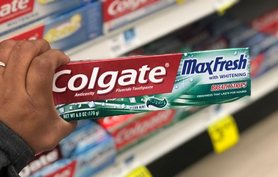 a womans hand holding a tube of colgate max fresh