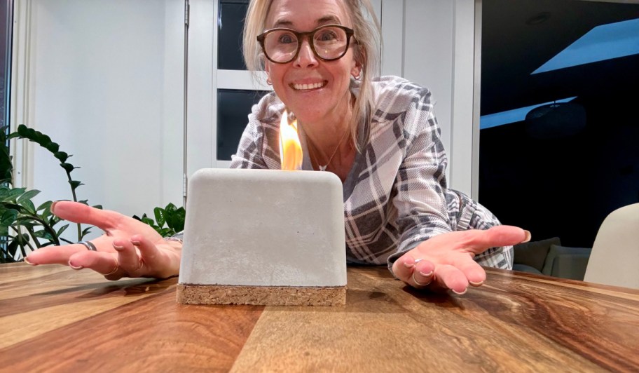 smiling woman standing behind a concrete tabletop firepit that's burning