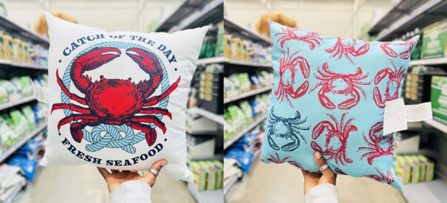 a womans hand holding up a crab throw pillow on a store aisle