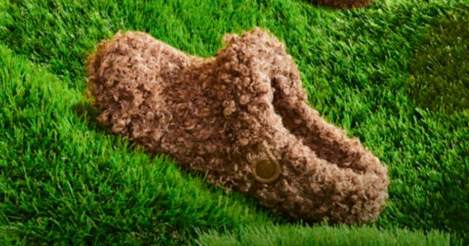 a crocs shoe with faux golden doodle dog like fur on the outside and inside, sitting outside in the grass