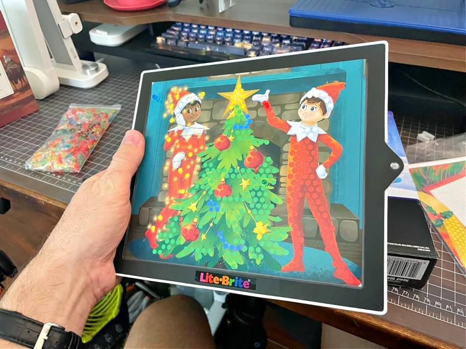 A hand holding an Elf on The Shelf Lite Brite toy.
