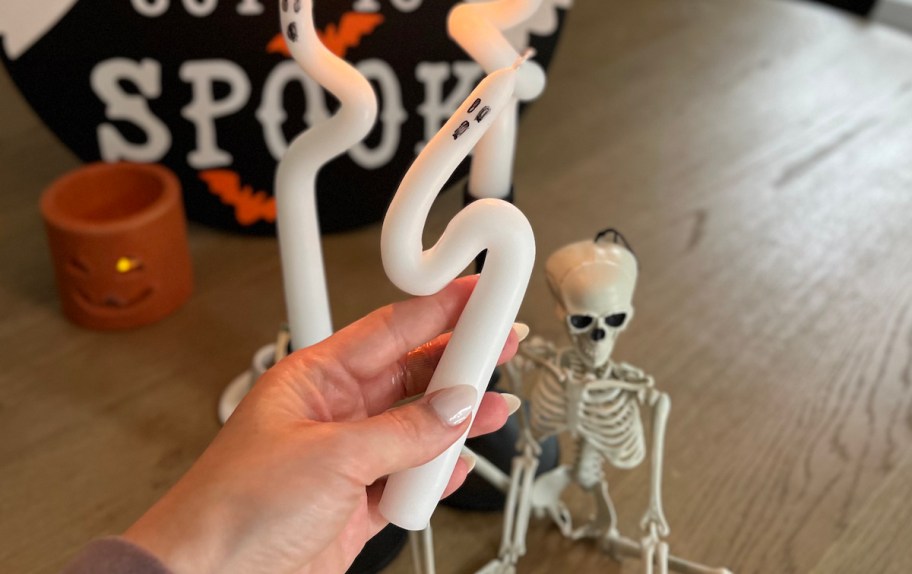 hand holding a ghost candle in front of skeleton on table