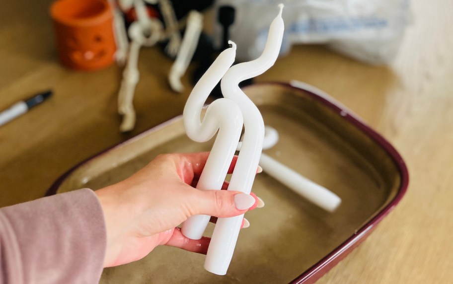 hand holding white taper candles over casserole dish of water