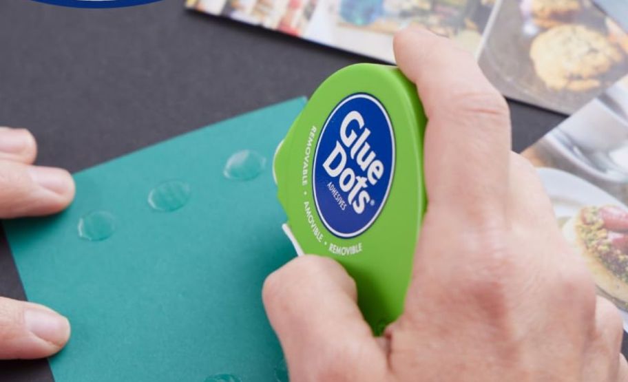 a hand holding a glue dots dispenser to a sheet of paper