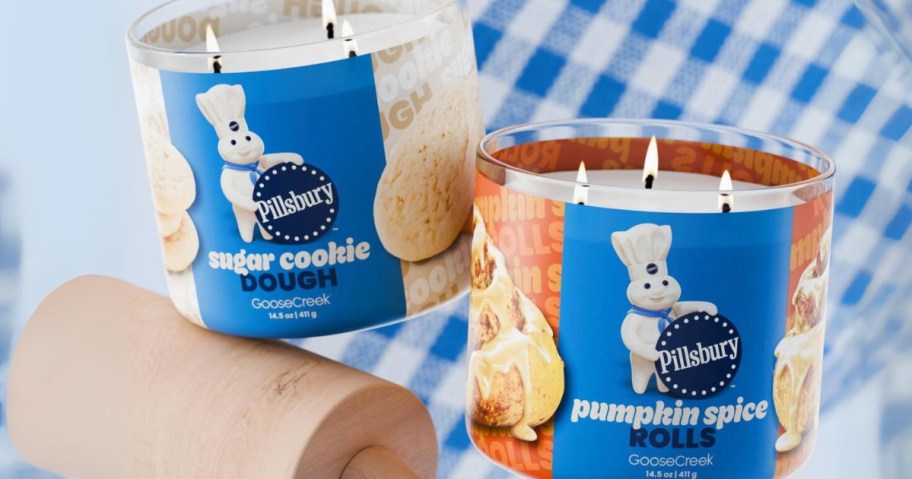 2 large jar candles with blue labels and a picture of the Pillsbury Dough Boy and a food item, rolling pin and blue and white checkered cloth behind them