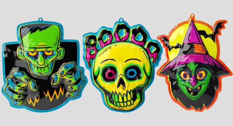 three pastic molded halloween themed signs; Frankenstein's Monster, a skull and a witch all in a neon color palette
