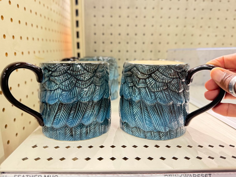 hand reaching for blue mugs on shelf 