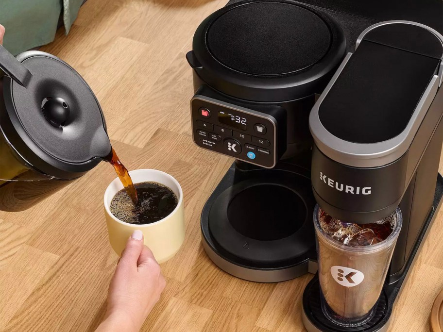 person pouring coffee into mug on table with keurig coffee maker