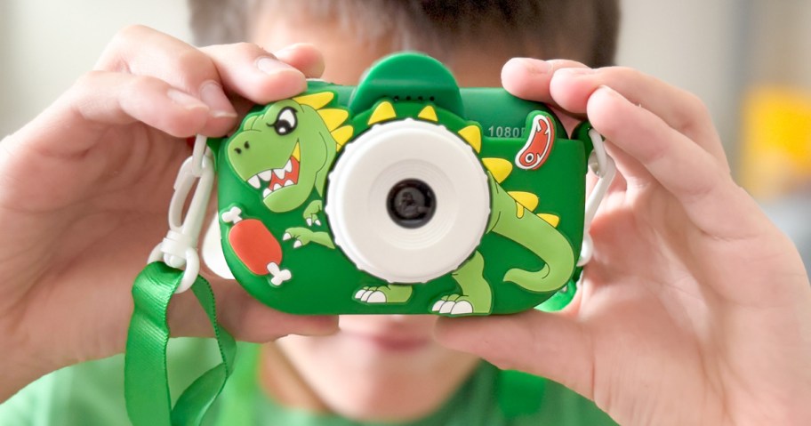 child holding a green dinosaur digital camera