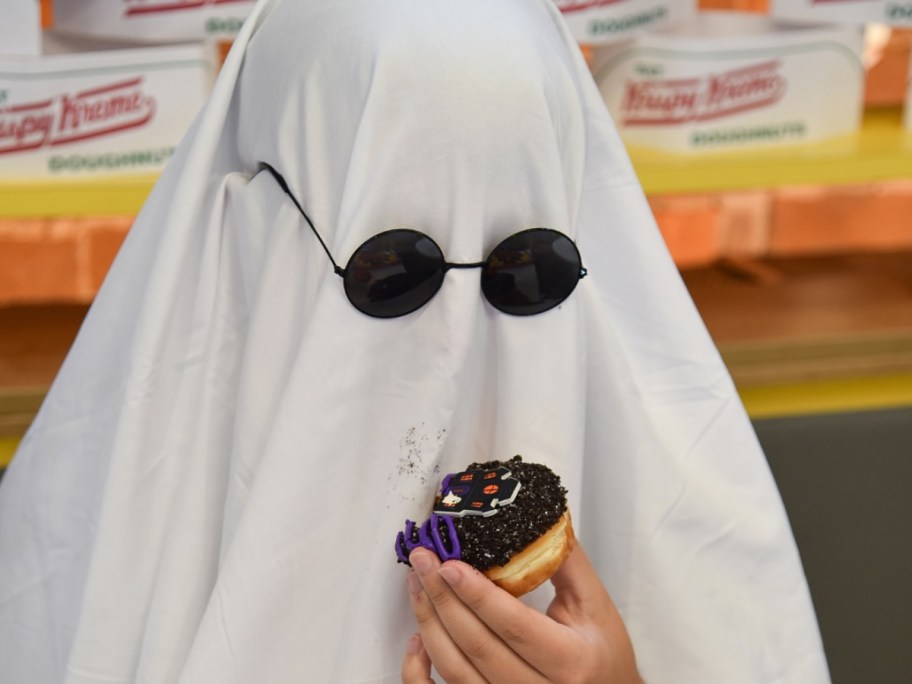 person in ghost costume wearing sunglasses and eating donut