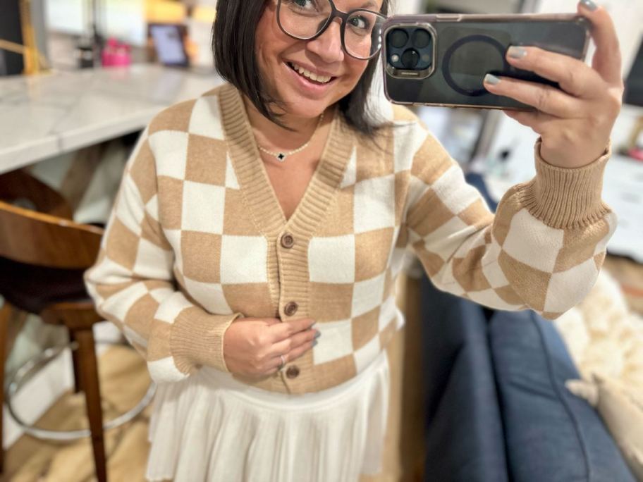 woman taking selfie in mirror wearing beige and white checked cardigan