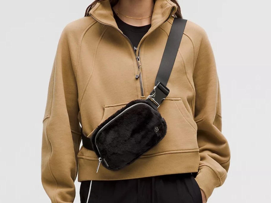 woman wearing a quarter zip tan color pullover with a black and gold fleece belt bag as a crossbody bag