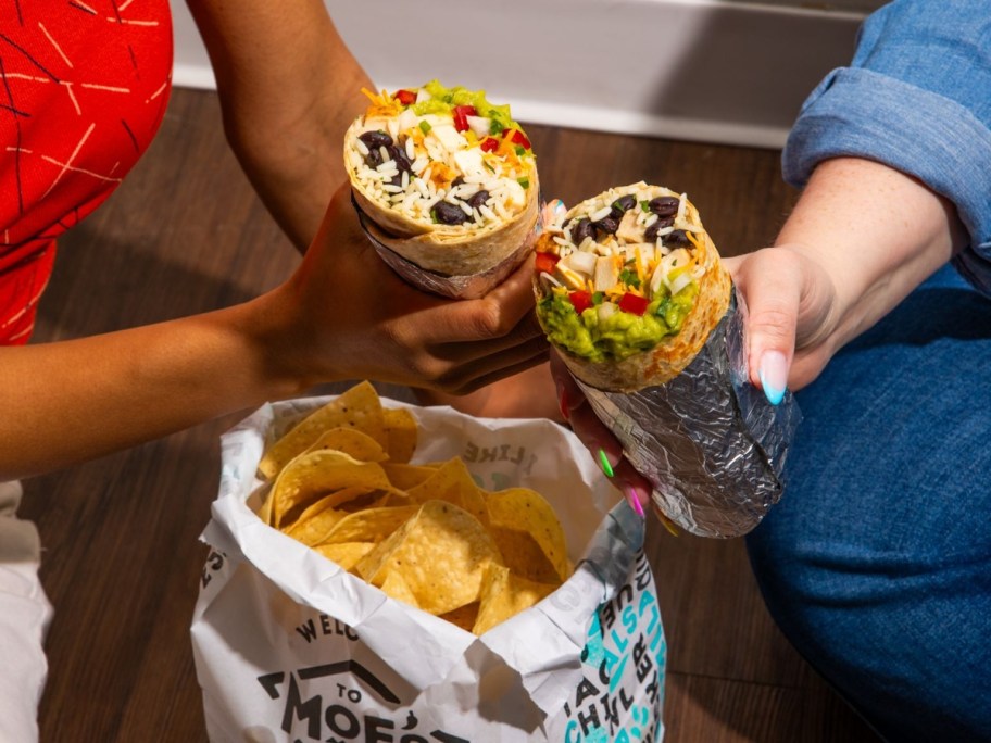 holding 2 burritos over a bag of chips from Moe's