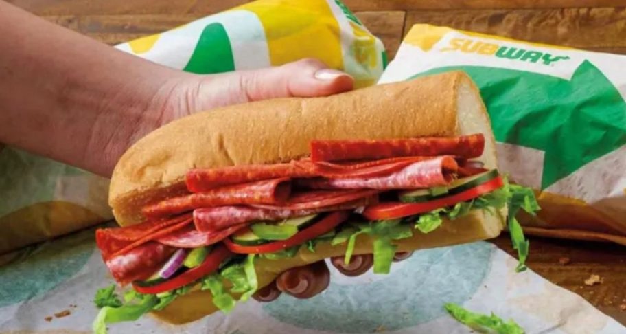 A hand holding a 6 inch subway sandwich