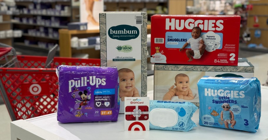 A display of various baby products including diapers, pull-ups, and wipes. There are packages of Huggies Snugglers, Pull-Ups, and Little Swimmers along with a package labeled bumbum. A Target gift card is also visible in the arrangement.