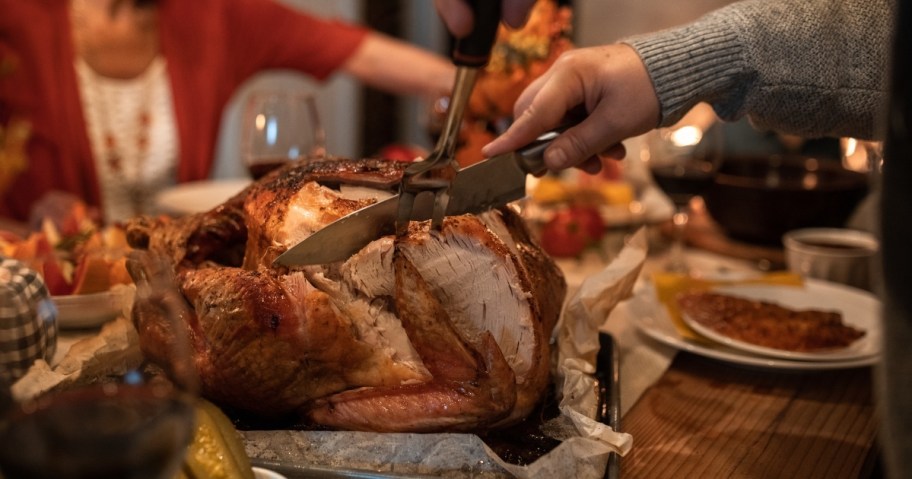 hands holding knives cutting into whole thanksgiving turkey at table