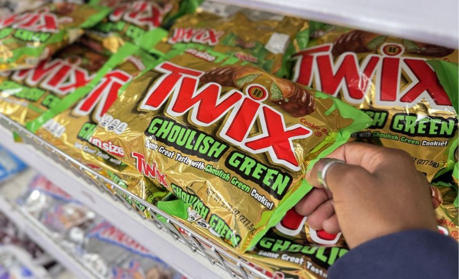 a womans hand holding a bag of twix ghoulish green candies