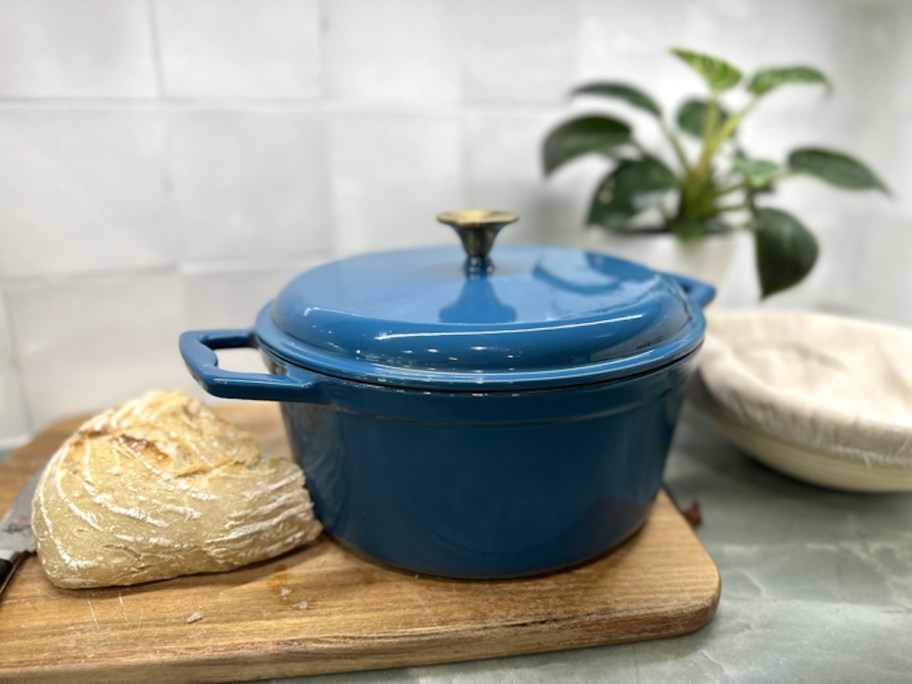 blue dutch oven on cutting board next to loaf of sourdough