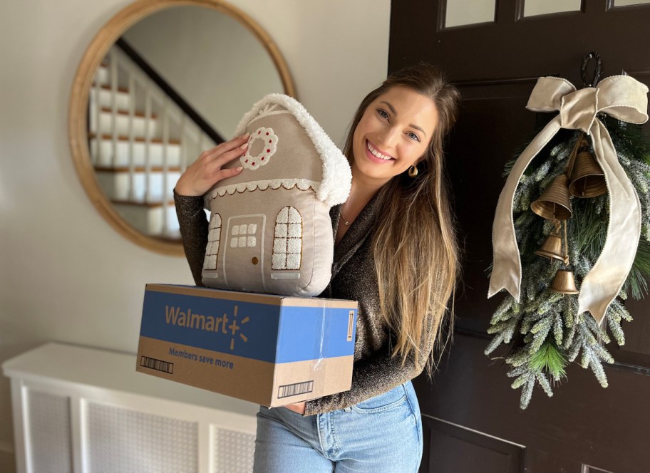 woman holding gingerbread house pillow with walmart box by front door