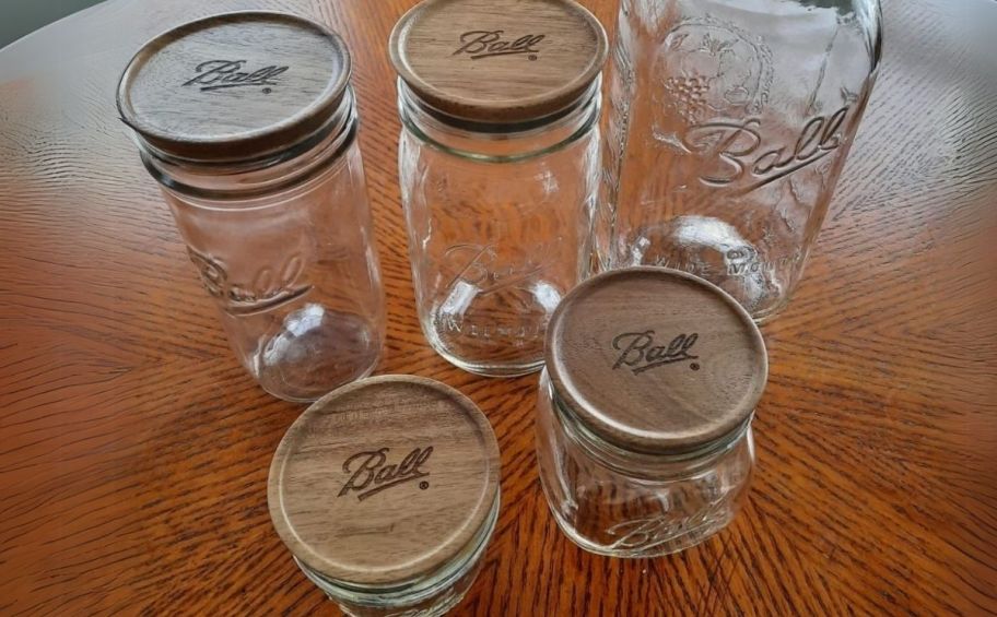 five glass canning jars with wooden lids sitting on a tabletop