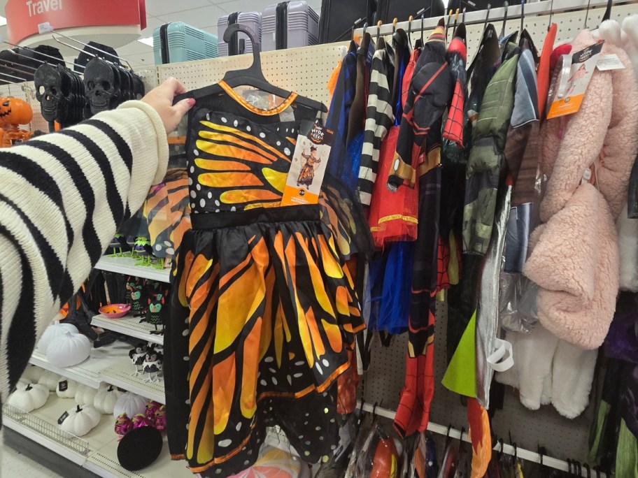 hand holding up a kids butterfly Halloween costume, more Halloween costumes on a store aisle behind it