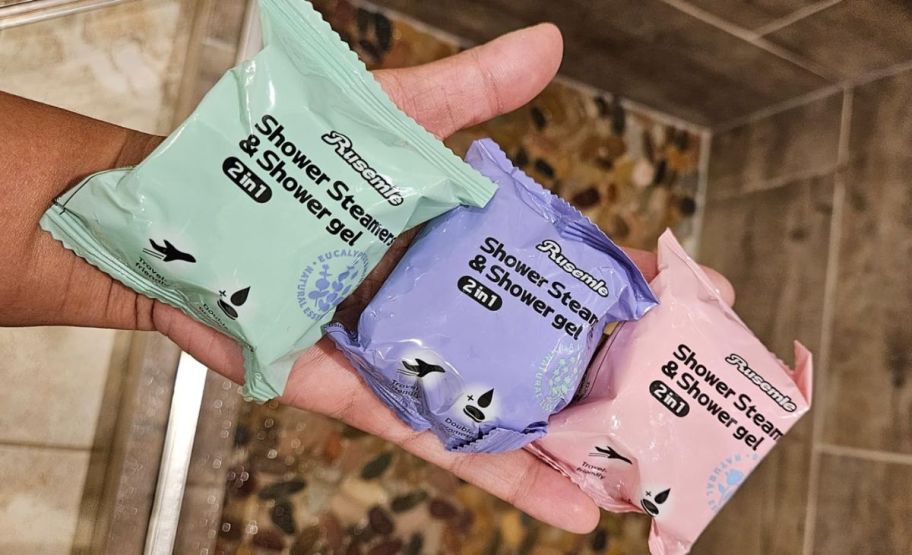 a womans hand holding three 2-in-1 shower steamer body wash packets