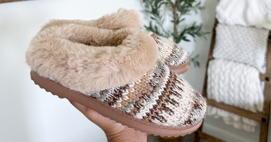 hand holding a pair of women's clog style slippers with a fair aisle print and faux fur