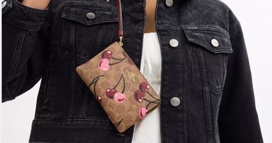 A woman holding a Coach Wristlet in Cherry Print