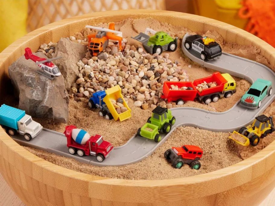 A barrel with sand filled with several Driven by Battat Mini Car Blind Bag Vehicles