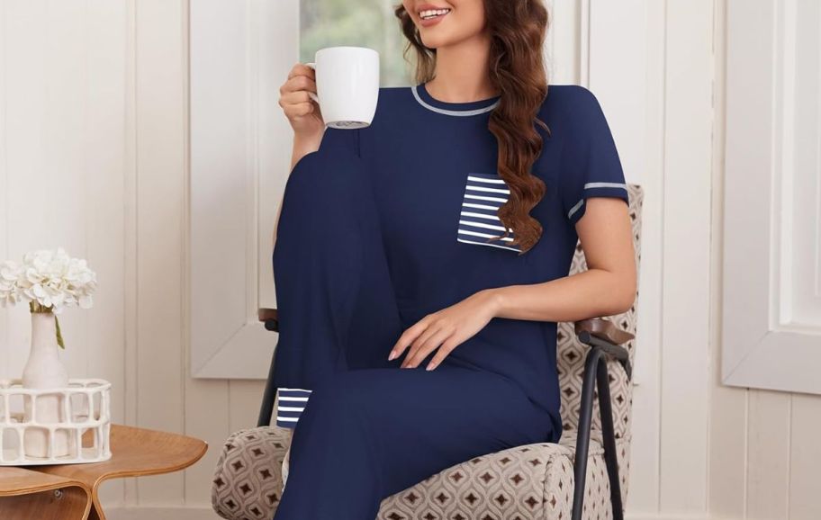 a woman seated and holding a coffee cup wearing a navy blue set of pajamas.