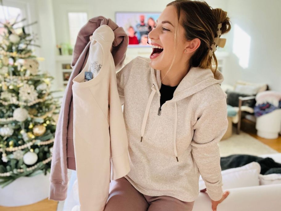 Woman holding a couple of fruit of the Loom sweatshirts while wearing one