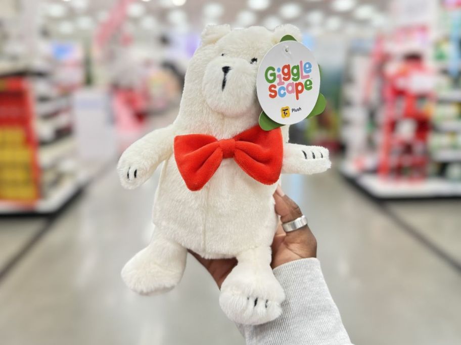 a womans hand holding a gigglescape plush bear in a red bowtie