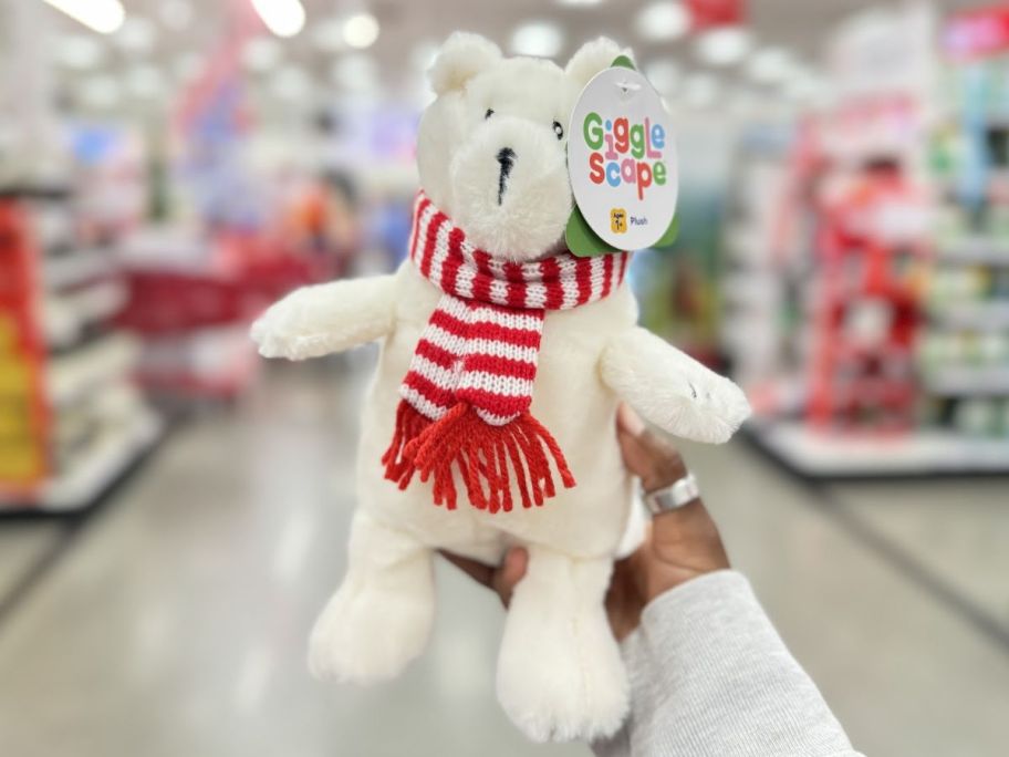 a womans hand holding a gigglescape plush bear in a red and white striped scarf