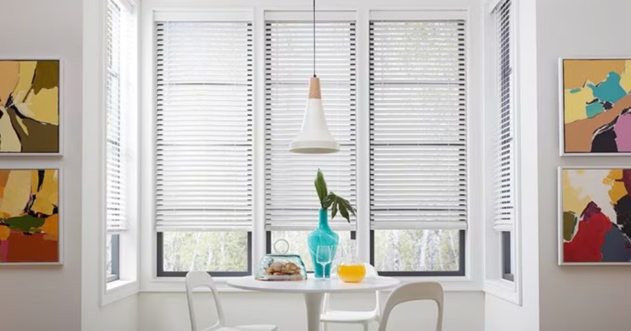 a dining room with a white table and chairs and windows behind it with white blinds on them