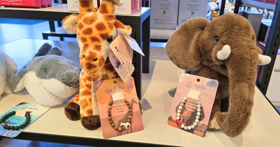 a plush shark, giraffe, and Elephant with beaded bracelets in front of them in a store