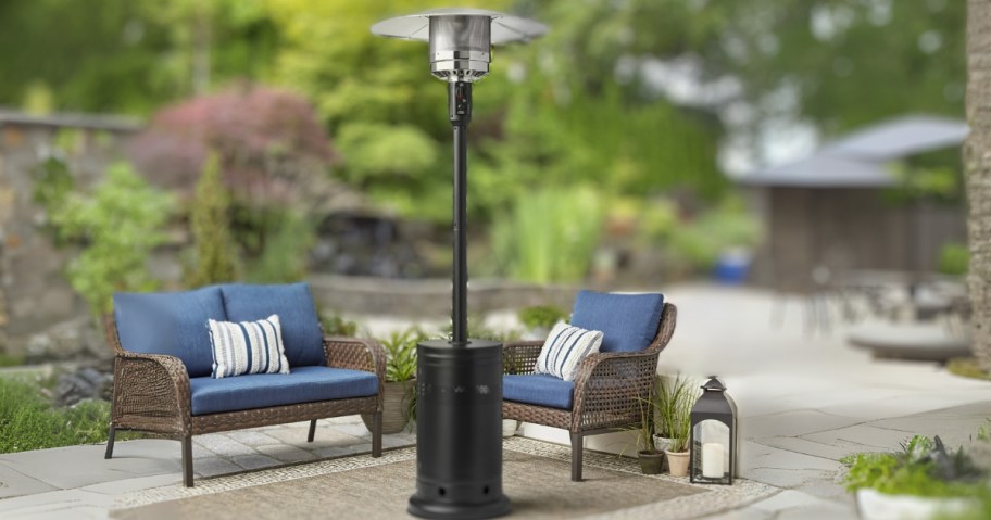 a black metal tall patio heater on a back patio with brown wicker furniture with blue cushions behind it