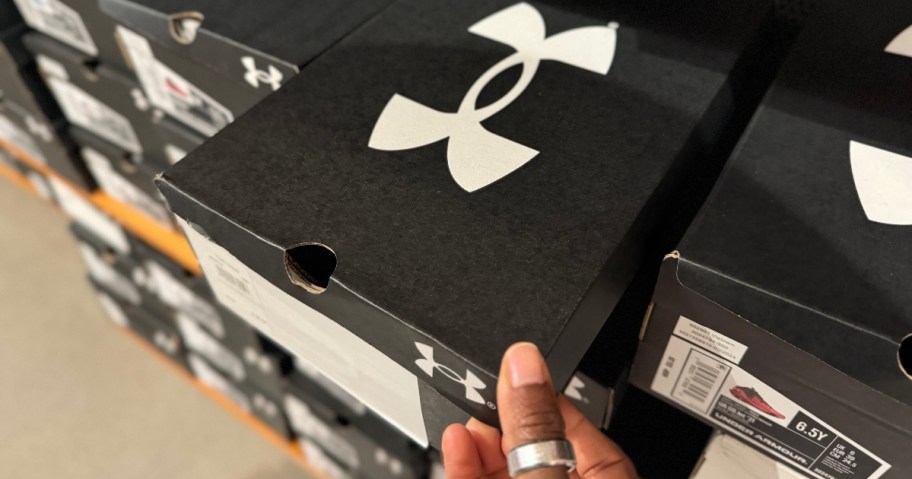 hand pulling a black and white Under Armour shoe box out of a wall display of them