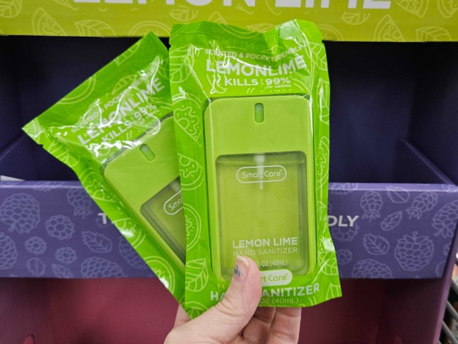 hand holding 2 green color hand sanitizers in the packaging they come in