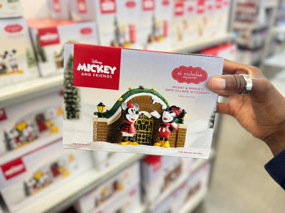 hand holding a box with a Disney Christmas Village piece in it of Mickey & Minnie Mouse by a gate