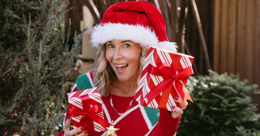 woman wearing a santa hat while holding two christmas gift boxes