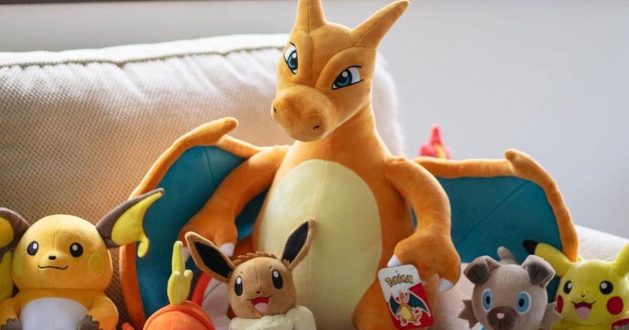 A Jumbo Charizard Plush next to smaller Pokemon plush on a couch