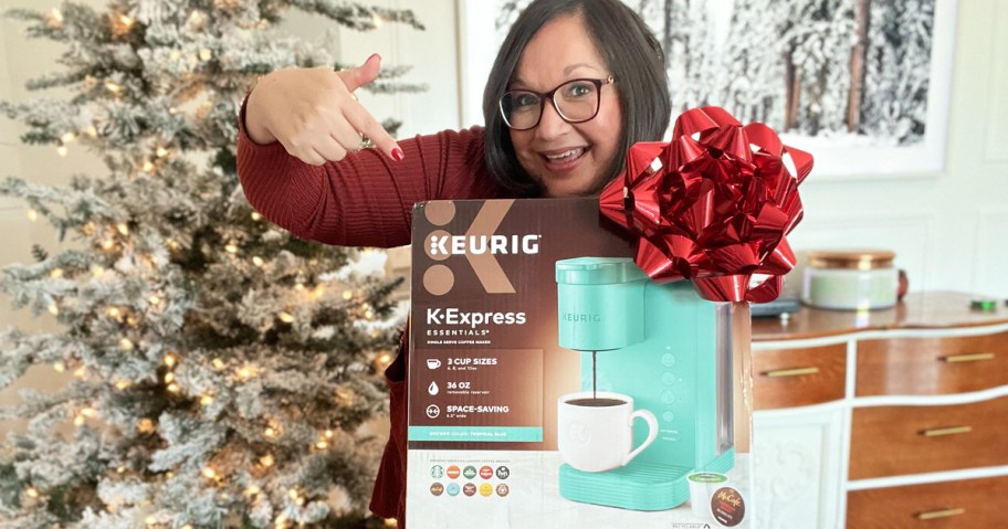 woman holding up box for Keurig K-Express Coffee Maker with a red bow on it in front of christmas tree