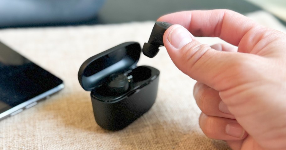 hand putting a small black earbud into a black charging case