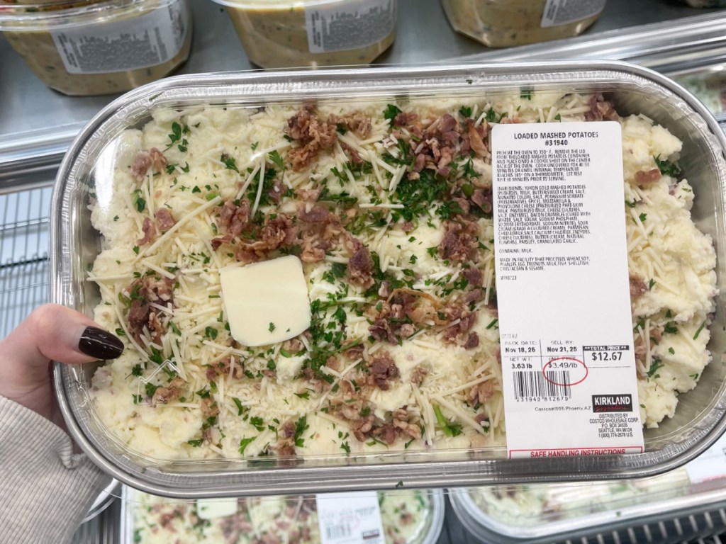 Woman holding container of loaded, mashed potatoes in hand