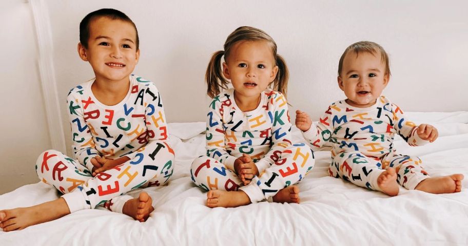 3 Sweet kiddos sitting on a bed wearing Old Navy Alphabet Pajamas 