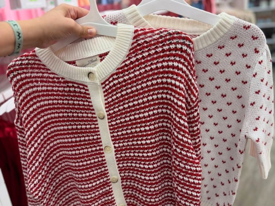 Hand holding hangers with CValentine's Day sweaters from Target