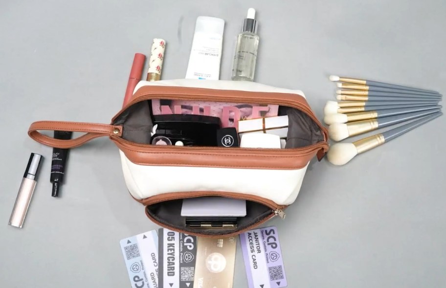 a white and tan makeup bag open showing items in it and more items around it that are about to be placed inside