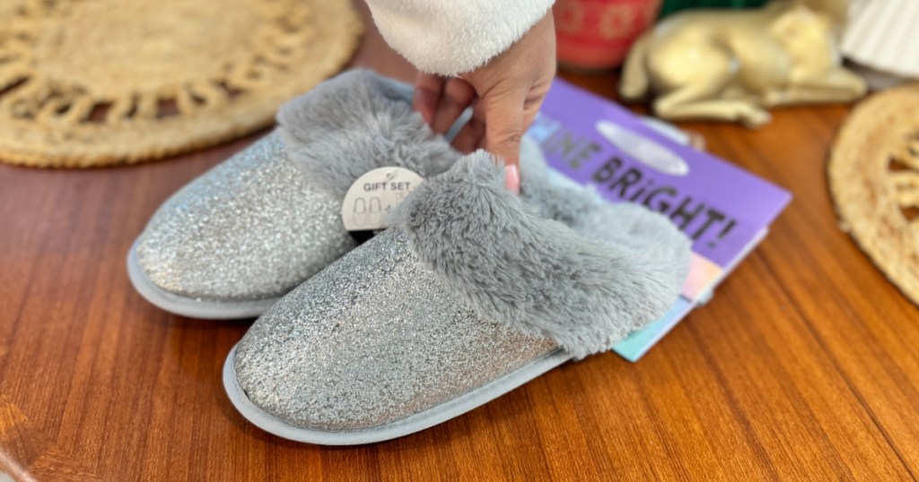 woman holding pair of silver glitter slippers