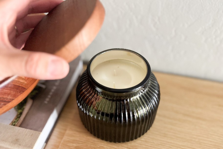 hand pulling lid of green ribbed candle