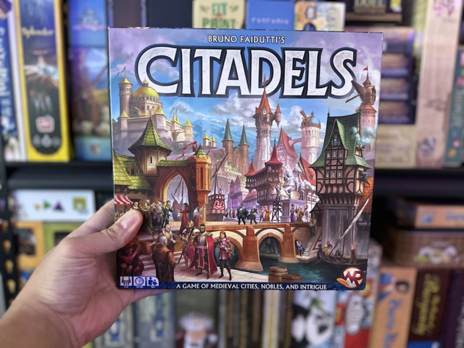 hand holding citadels board game in front of shelf